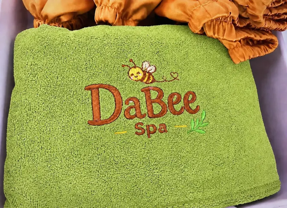 Khăn màu xanh thêu logo DaBee Spa cùng trang phục dành cho khách